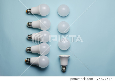 Creative geometric composition with LED lights on a blue background. One bulb without a diffuser, five new whole bulbs, and three white matte light diffusers. Flat lay 75877342