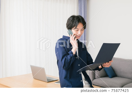 一個年輕人坐在客廳的桌子上,檢查材料 一個年輕人坐在客廳的桌子上,檢查材料 75877425