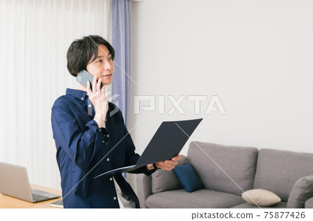一個年輕人坐在客廳的桌子上,檢查材料 一個年輕人坐在客廳的桌子上,檢查材料 75877426