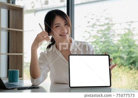 Business woman holding and pointing at digital tablet with blank screen in home office. Business woman holding and pointing at digital tablet with blank screen in home office. 75877573