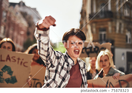 Emotional young woman screaming a slogan and leading a group of demonstrators on the road 75878323