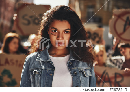 Women power. Afro american woman with word power written on her face protesting with group of female activists outdoors on road. 75878345