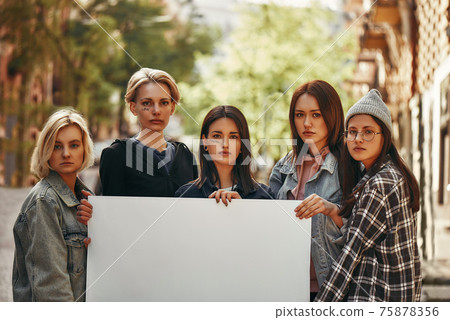 Group of protesting young female activists holding blank signboard and looking at camera while standing on the road Group of protesting young female activists holding blank signboard and looking at camera while standing on the road 75878356
