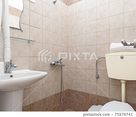 Closeup of simple style interior of small restroom with beige ceramic tile walls, white sink and classic WC toilet Closeup of simple style interior of small restroom with beige ceramic tile walls, white sink and classic WC toilet 75879741