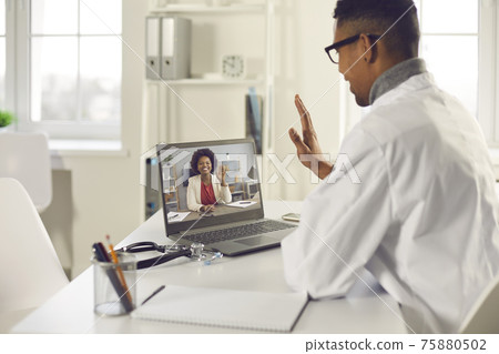 African american male doctor looking at laptop screen waving hand back view shot African american male doctor looking at laptop screen waving hand back view shot 75880502