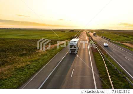 Truck with semi-trailer driving along highway on the sunset background.  75881322