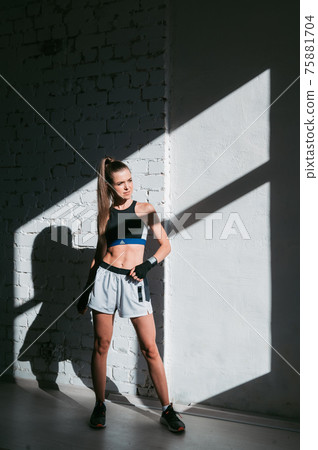 Beautiful contrasting portrait with the play of light and shadow of a young and fit girl in a loft interior with a white brick wall 75881704