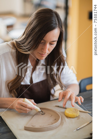 Craftsman hands connect the clay parts made of raw clay, master fingers work with pieces of clay, female sits at a workshop behind the table Craftsman hands connect the clay parts made of raw clay, master fingers work with pieces of clay, female sits at a workshop behind the table 75881744