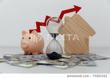 Piggy bank, hourglass with arrow up and wooden house models on dollar cash Piggy bank, hourglass with arrow up and wooden house models on dollar cash 75882042