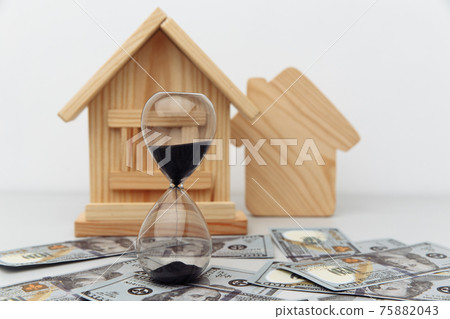 Wooden house and clock on dollar banknotes. Buying or selling real estate concept Wooden house and clock on dollar banknotes. Buying or selling real estate concept 75882043