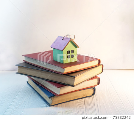 A stack of books or textbooks with a small decorative house with space for text. The concept of home education. A stack of books or textbooks with a small decorative house with space for text. The concept of home education. 75882242