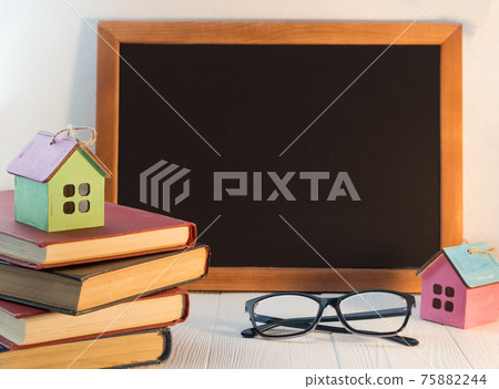 A stack of books or textbooks with a small decorative house and a blackboard with space for text. The concept of home education. 75882244