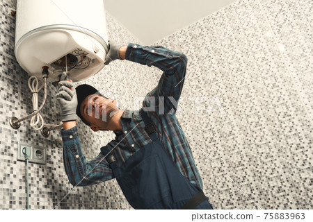 Plumber installing electric heating boiler. Young handyman in uniform setting up electric heating boiler at home 75883963