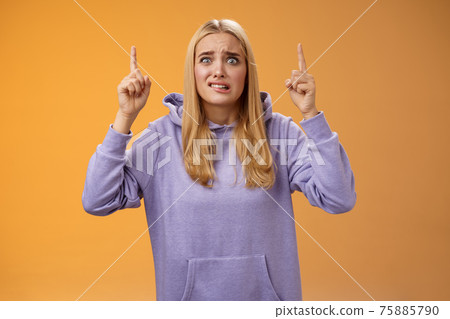 Worried perplexed unsure cute blond woman presenting project standing awkward afraid humiliation crining scared pointing up raised index finger waiting reply nervously, orange background 75885790