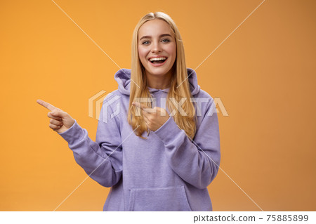 Charismatic firendly good-looking blond young female student pointing left discussing awesome new restaurant suggesting friend go check out laughing smiling happily, orange background 75885899