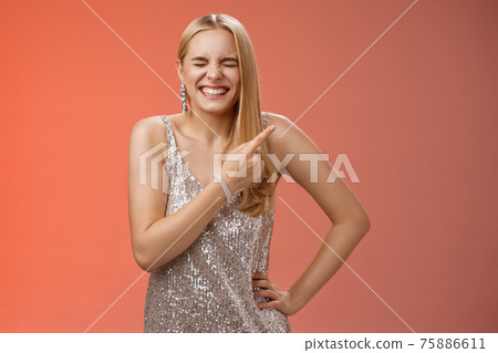 Carefree joyful blond attractive woman having fun joking laugh hilarious boyfriend outfit close eyes giggling smiling broadly pointing upper right corner behind standing red background 75886611