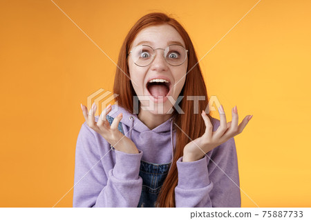 Shocked excited overwhelmed young screaming happy redhead girl wearing glasses winning hear excellent news yelling out loud rejoicing unbelievable luck raising hands spread stare surprised 75887733