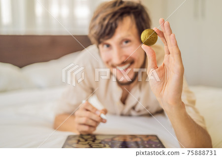 Young man, a digital artist, creates digital art on a tablet at home and shows a coin with the inscription NTF - non fungible token. Remote work, digital nomad, digital painting, animation, video 75888731