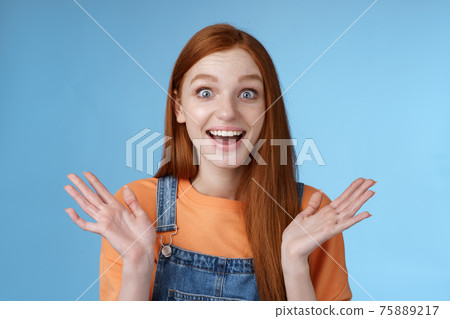 Surprised delighted happy friendly-looking amused redhead female friend learn incredible good news congratulating girlfriend fascinated wide eyes camera joyfully clap hands amazed, blue background 75889217