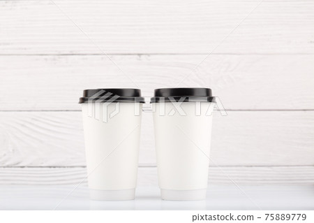 Two white tall disposable coffee cups on white table against white wooden background 75889779