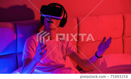 Young impressed man in virtual reality glasses at home Young impressed man in virtual reality glasses at home 75893258
