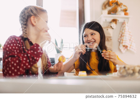 Two sisters are sitting at the table and painting Easter eggs in different colors for Easter, close-up 75894632