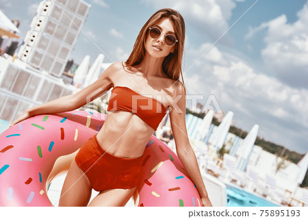 To keep the body in good shape is a duty. Sexy woman is wearing red bikini and holding inflatable swim ring in shape of donut To keep the body in good shape is a duty. Sexy woman is wearing red bikini and holding inflatable swim ring in shape of donut 75895193