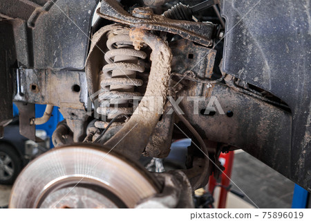 Inspects shock absorber, springs and stabilizer bars with a flashlight. Car on a repair stand. Technical service station for car. 75896019