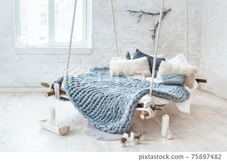 White loft interior in classic scandinavian style. Hanging bed suspended from the ceiling. Cozy large folded gray plaid, giant knit blanket, super chunky yarn, arm knitting. Trendy room design. 75897482