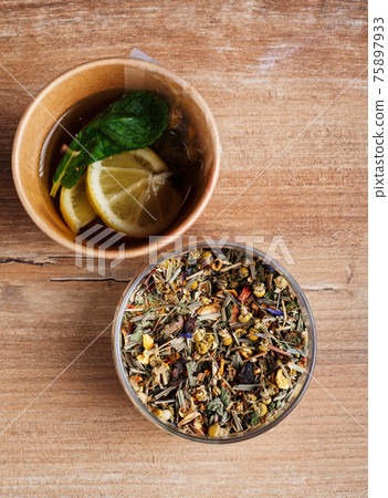 Glass of tea leaves and brewed tea with lemon and mint in a disposable paper cup on a wooden rustic background. Top view. 75897933