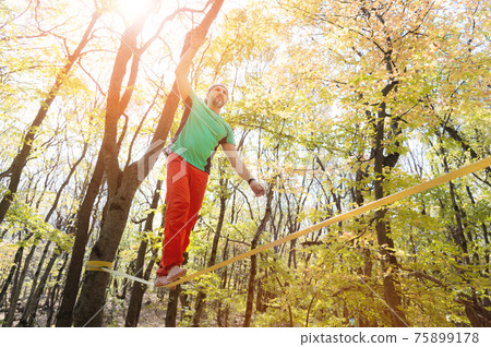 Autumn forest. middle aged athletic man practices slackline balance in autumn forest. 75899178