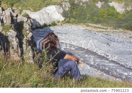 A man sits on a mountainside and looks at a stormy river A man sits on a mountainside and looks at a stormy river 75901223