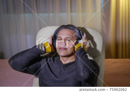 50-year-old man listens to music on headphones at home, sitting in a chair. 50-year-old man listens to music on headphones at home, sitting in a chair. 75902062