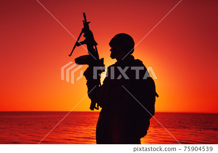 Army machine gunner patrolling beach at sunset 75904539