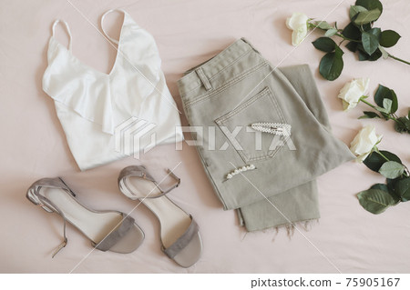 Overhead view of woman's casual spring summer outfit. Jeans, white blouse, sandals and bouquet of flowers on beige background. Flat lay, top view. 75905167