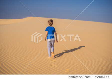 Young boy traveling in the desert. Sandy dunes and blue sky on sunny summer day. Travel, adventure, freedom concept. Tourism reopens after quarantine COVID 19 75906143
