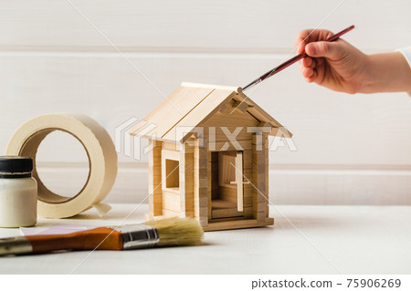 Child hands with toy wooden house and paint brush, home services concept Child hands with toy wooden house and paint brush, home services concept 75906269