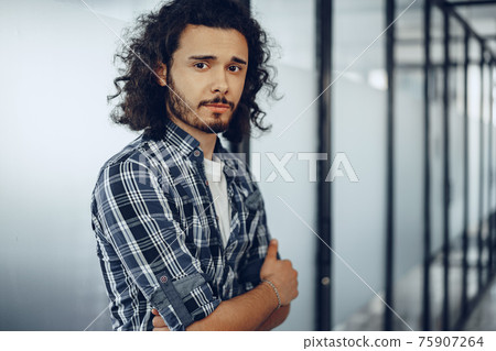 Portrait of young curly casually dressed male entrepreneur standing in a glass corridor 75907264