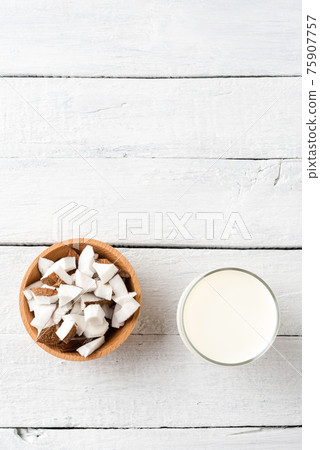 Glass of coconut milk on white wooden background with coconut pieces and copyspace. Top view Glass of coconut milk on white wooden background with coconut pieces and copyspace. Top view 75907757