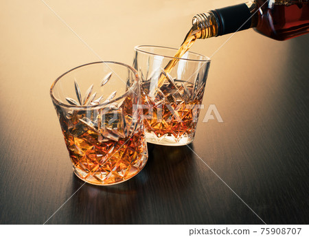 whiskey is poured into a glass from bottle 75908707