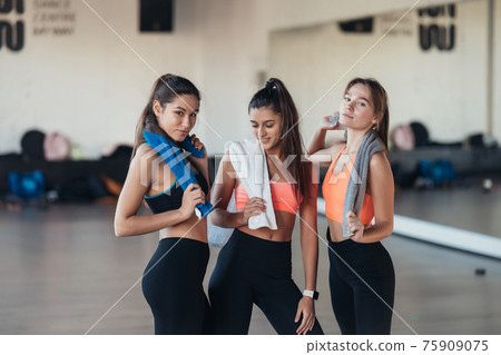 Three happy smiling positive girls after training in the gym. 75909075
