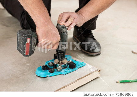 A tiler uses a caliper with a suction cup to drill holes in the ceramic tile. 75909862