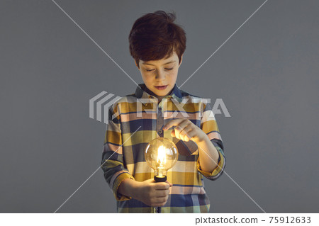 Boy touching glowing lightbulb lamp in hand stand isolated on studio copy space 75912633
