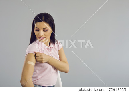 Woman looking at medical patch on hand standing over studio copy space 75912635