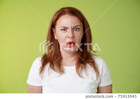Confused shocked gasping middle-aged redhead woman cringe frustrated puzzled open mouth speechless freak out strange shocking scene stand green background perplexed disappointed Confused shocked gasping middle-aged redhead woman cringe frustrated puzzled open mouth speechless freak out strange shocking scene stand green background perplexed disappointed 75913043