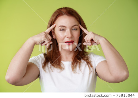 Smart choice. Intrigued thoughtful good-looking assertive redhead creative middle-aged woman touch temples squinting pondering info thinking use mental power read minds stand green background 75913044