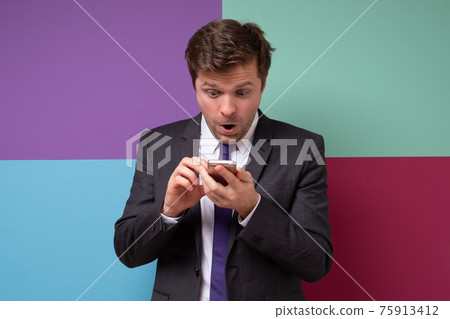 Young man in suit looking excited holding his smartphone pointing on screen Young man in suit looking excited holding his smartphone pointing on screen 75913412