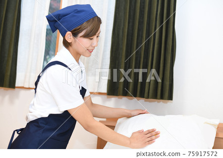 A woman who is a housekeeper who makes a bed 75917572