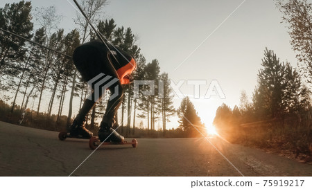 Training an athlete on the roller skaters. Biathlon ride on the roller skis with ski poles, in the helmet. Autumn workout. Roller sport. 75919217