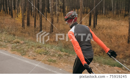 Training an athlete on the roller skaters. Biathlon ride on the roller skis with ski poles, in the helmet. Autumn workout. Roller sport. Training an athlete on the roller skaters. Biathlon ride on the roller skis with ski poles, in the helmet. Autumn workout. Roller sport. 75919245